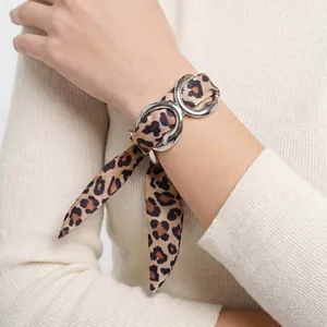 Detail of stainless steel geometric open bracelet with leopard print silk scarf on wrist