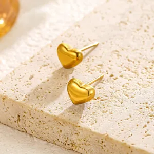 Close-up of golden heart-shaped stud earrings on a textured stone surface