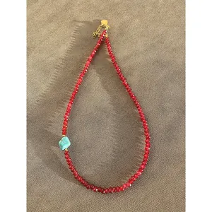 Close-up detail showing the faceted red beads and the turquoise stone on the necklace