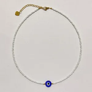 Detailed view of handmade white seed bead necklace featuring a blue glass evil eye charm.