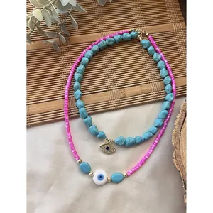 Detail view of turquoise and pink beaded necklaces with evil eye charms on bamboo mat.