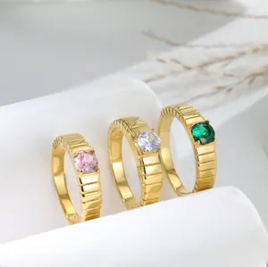 Dettaglio di tre anelli dorati testurizzati con gemme di colore rosa, bianco e verde