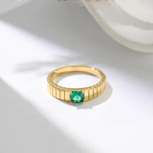 Primo piano di un anello dorato con texture verticale e dettaglio in pietra verde smeraldo.