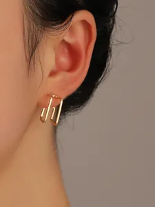 Detail view of double-layered geometric gold rectangular earrings on a model's ear