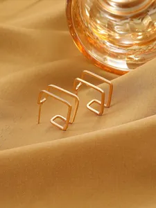 Detail shot of gold minimalist geometric square earrings on warm fabric