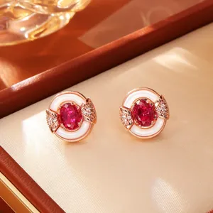Macro detail of rose gold stud earrings with oval red gemstone and white pearl inlay.