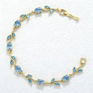 Elegant gold leaf branch bracelet with light blue gemstones on textured white background.