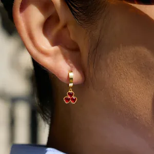 Close-up of 18K gold plated titanium earrings featuring a red stone clover charm.