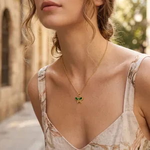 Detailed view of a delicate gold butterfly necklace with green zircon on a model's neck