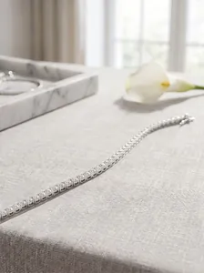 Macro detail of a shimmering sterling silver tennis bracelet on a linen surface