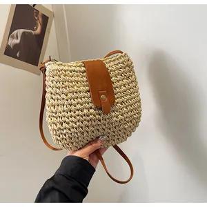 Nahaufnahme einer stilvollen Stroh-Eimertasche mit brauner Lederklappe und Gurt.