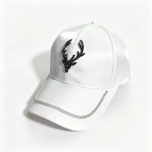 Detailed view of white satin baseball cap with black rhinestone deer head and chain trim.