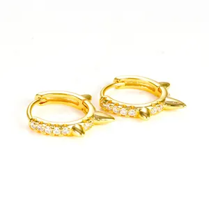 Macro view of gold-toned huggie hoop earrings featuring spikes and clear CZ stones