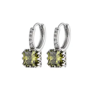 Close-up of silver hoop earrings featuring square olive green gemstones and pave stones.