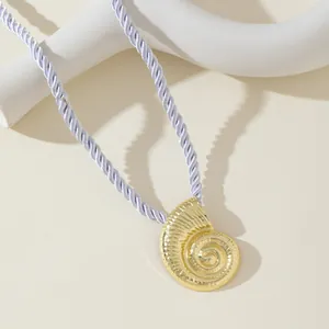 Detalle macro de un colgante de nautilus dorado con un cordón de seda trenzado morado