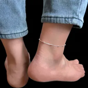 Detailaufnahme eines minimalistischen Fußkettchens aus silbernem Titanstahl an einem Knöchel