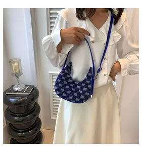 Detail of a woman wearing a blue and navy checkered crescent shoulder bag with frayed edges.