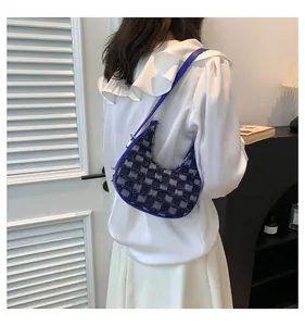 Model wearing a stylish blue checkered crescent underarm bag in a minimalist interior setting