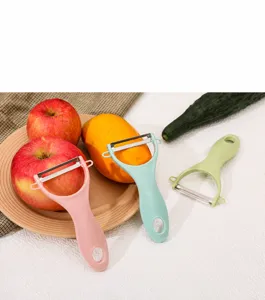 Trio di pelapatate in ceramica colorati con mele e mango freschi in un contesto di cucina.