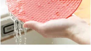 Détail du tapis isolant en silicone rose nettoyé sous un jet d'eau dans un évier