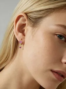 Gros plan de boucles d'oreilles créoles fleurs avec zircons roses portées par un mannequin.