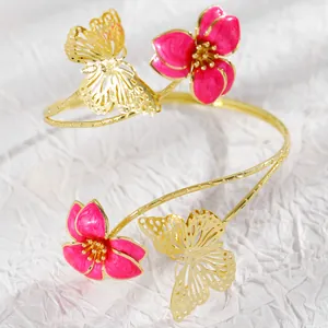 Close-up of golden arm cuff featuring pink enamel flowers and filigree butterflies
