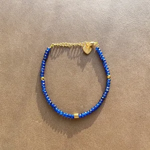 Detailed view of deep blue faceted natural stone beaded bracelet featuring a gold heart charm