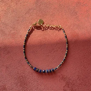 Detail view of blue natural stone beaded bracelet with golden heart charm on red surface