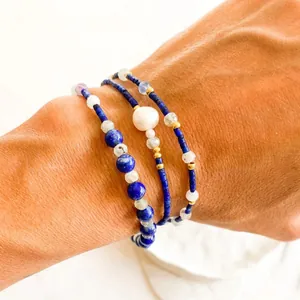 Detailed view showing a layered blue lapis lazuli and pearl beaded bracelet on a wrist