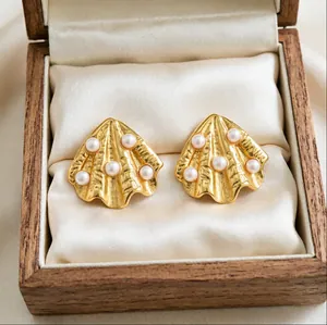 Detailed close-up of golden shell-shaped earrings with pearl accents inside a wooden box