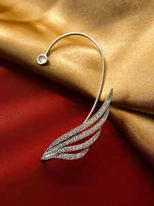 Detail view of a sparkling silver wing ear cuff with zircon on satin background.
