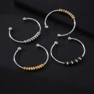 Detalle de pulseras abiertas de hilo de acero inoxidable con cuentas doradas, negras y plata.