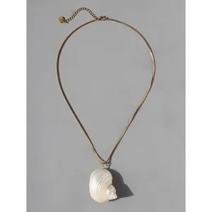 Elegante goudkleurige ketting met witte natuurlijke schelphanger op een grijze basis