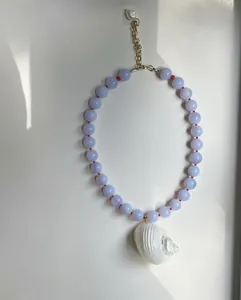 Detailweergave van een handgemaakte ketting met een witte schelphanger en paarse kralen.