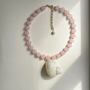 Close-up van roze kralenketting met een grote iriserende witte schelphanger aan de ketting.