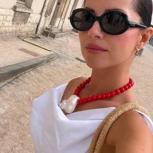 Detailweergave van een rode kralenketting met een witte schelphanger gedragen door een model