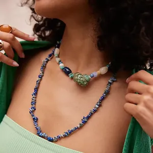 Detail van gelaagde parel- en lapis lazuli-kettingen met een groene schelp hanger