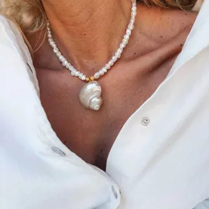 Close-up van een minimalistische zoetwaterparelketting met een grote iriserende schelphanger
