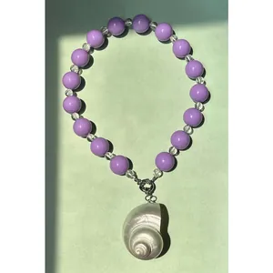 Detail van een paarse kralenketting met een grote iriserende schelp hanger