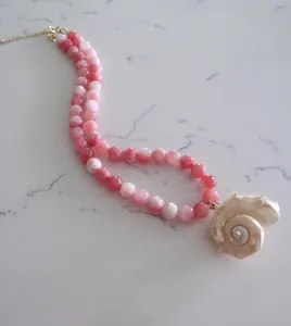 Detail van een roze kralenketting met een hanger van een natuurlijke zeeschelp