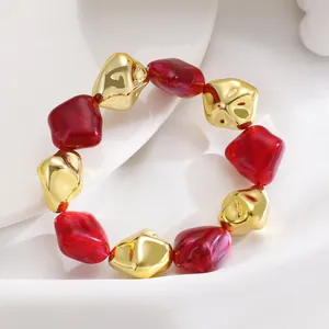 Close-up view of chunky irregular red resin and gold beads bracelet on white fabric