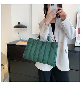 Close-up of a stylish dark green quilted tote bag held by a model wearing a white blazer.