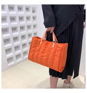 Orange quilted puffy tote bag held by model for autumn winter fashion