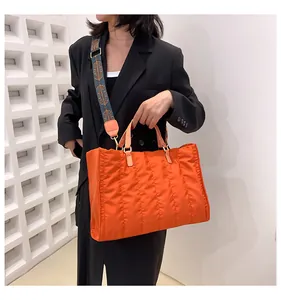 Model carrying a large orange quilted tote bag with a patterned strap for commuting.
