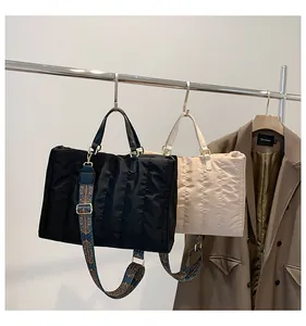 Fashionable quilted tote bags in black and beige hanging on a rack with patterned straps.