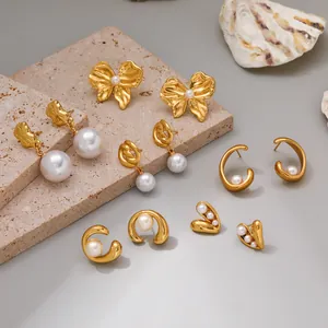 Collection of elegant gold stainless steel earrings with pearl details on a stone slab