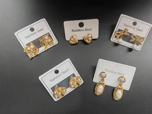 Primo piano di vari orecchini di perle in acciaio inossidabile con fiocchi e cuori.