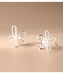 Primo piano di orecchini a fiore in argento con perle su sfondo beige caldo.