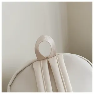 Close-up view of the reinforced top handle and shoulder straps on a minimalist beige backpack.