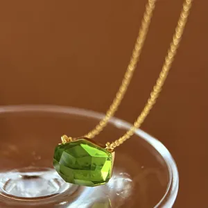 Macro view of a minimalist irregular cut green gemstone pendant with a gold chain.